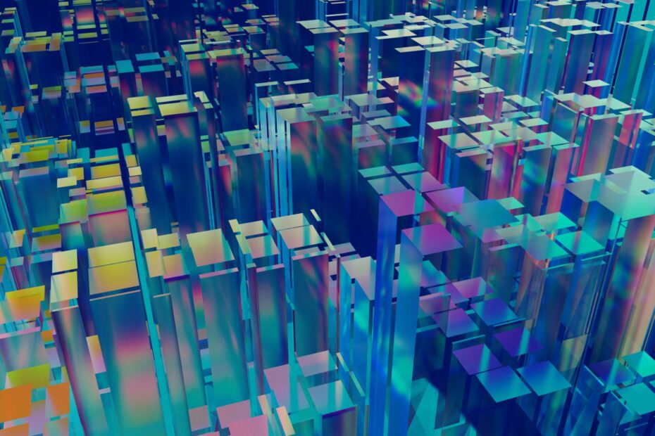 A colorful abstract 3D cityscape composed of translucent, multicolored blocks arranged in various heights and orientations. The blocks create a visually striking, futuristic landscape with a mix of blue, green, purple, and yellow hues, giving the impression of a digital or virtual environment. The overall effect is vibrant and dynamic, suggesting complexity and depth.