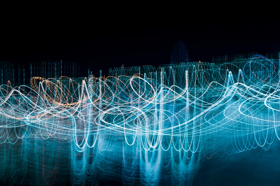 Abstract light trails in blue and white against a dark background, creating a dynamic, wave-like pattern that suggests movement and energy.