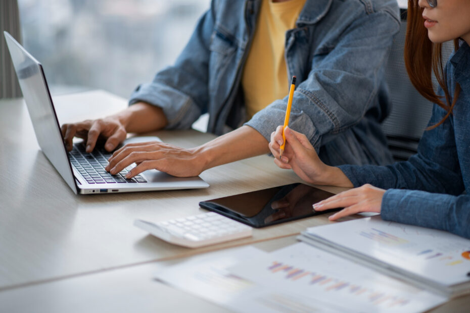 Two professionals collaborating at an Android app development agency, working on a laptop and tablet with data charts and reports on the desk, showcasing teamwork and innovation in mobile app development